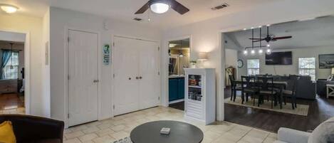 A living room with a ceiling fan, a dining area with a table and chairs, and a kitchen area with cabinets and a refrigerator.