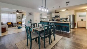 A modern kitchen with a central island, pendant lighting, and a dining area with a table and chairs. - The Gulf Breeze Getaway (Gulfport)