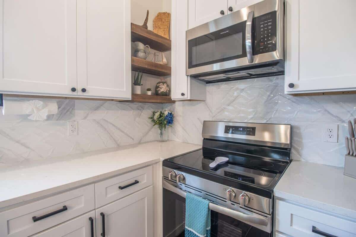 A kitchen with white cabinets, a stainless steel microwave, an oven, and a built-in stove.