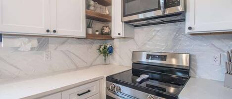 A kitchen with white cabinets, a stainless steel microwave, an oven, and a built-in stove.