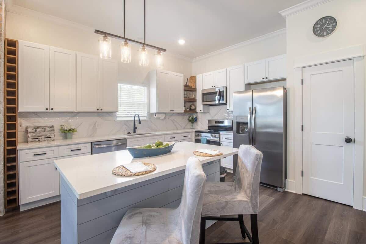 A modern kitchen with white cabinets, a stainless steel refrigerator, and a central island with chairs.