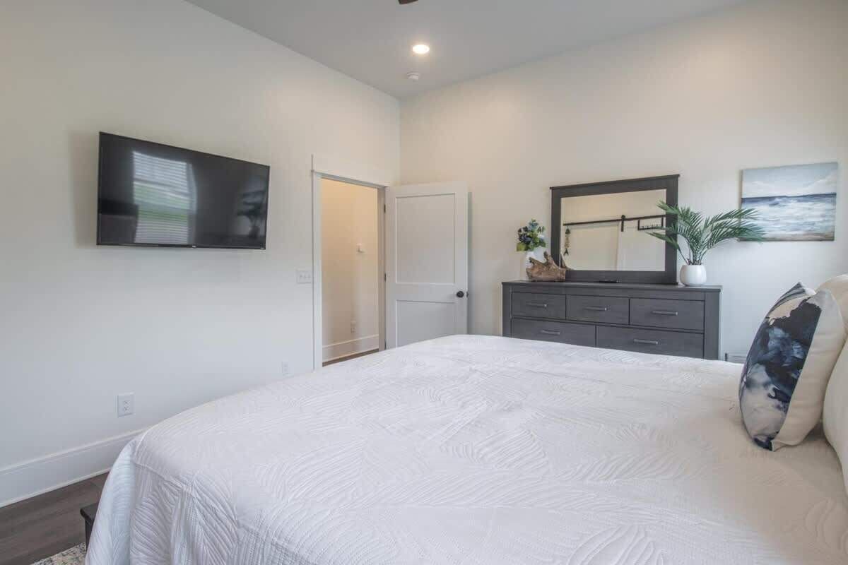 Un dormitorio con cama, cómoda, televisor, puerta y un cuadro en la pared.