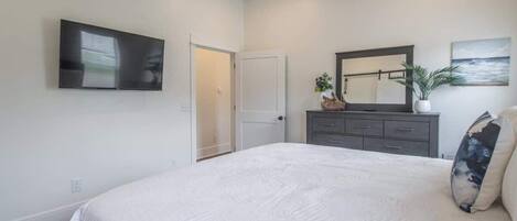 A bedroom with a bed, a dresser, a television, a door, and a painting on the wall.