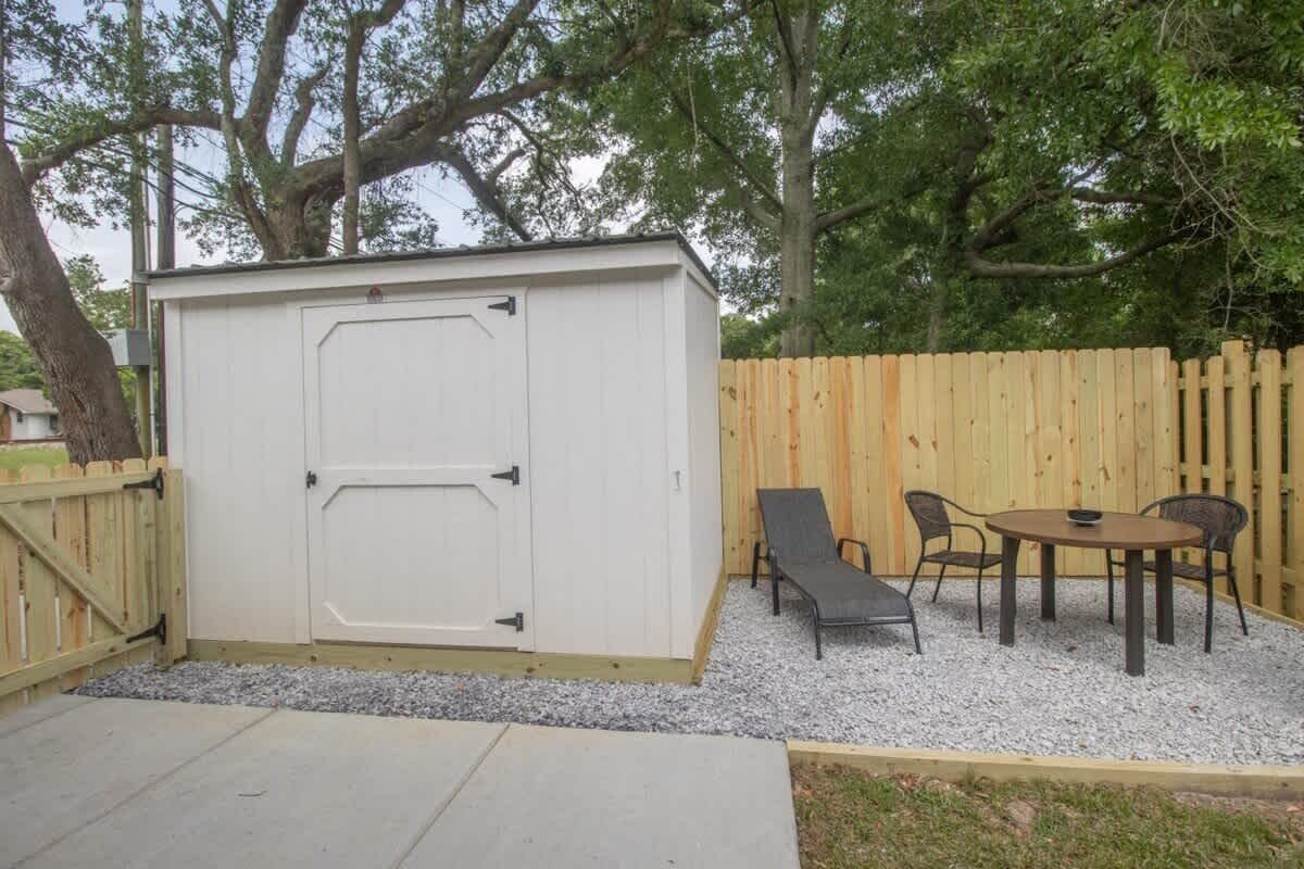 A small shed with a door, a wooden fence, and a patio area with a table and chairs.
