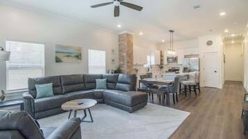 A modern living room with a sectional sofa, a dining area, and a kitchen in the background.