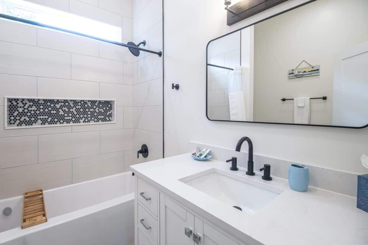 A modern bathroom with a white sink, black faucet, and a large mirror.