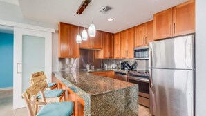 Una cocina moderna con encimeras de granito, electrodomésticos de acero inoxidable, armarios de madera e iluminación colgante.