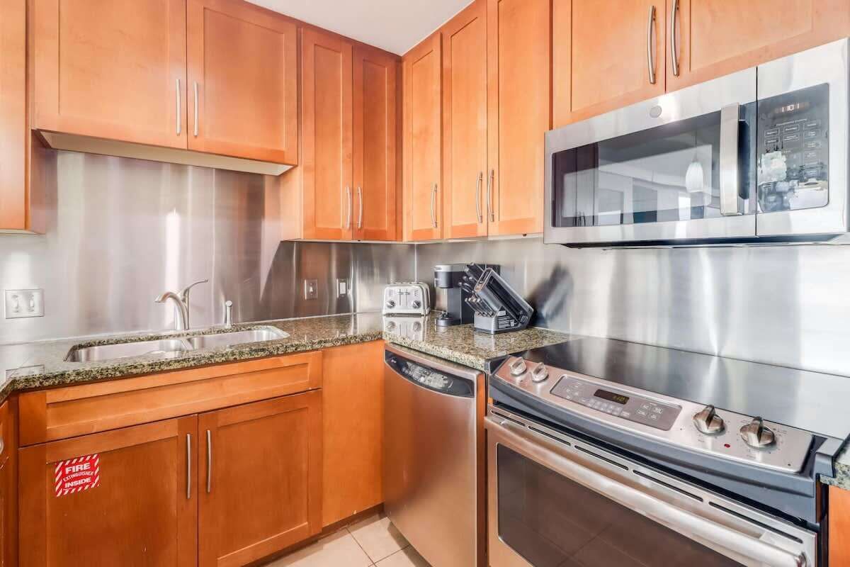 Een keuken met houten kastjes, een RVS magnetron, een ingebouwde oven en een vaatwasser.
