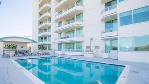 Una piscina junto a un hotel de varios pisos con balcones y ventanas amplias.