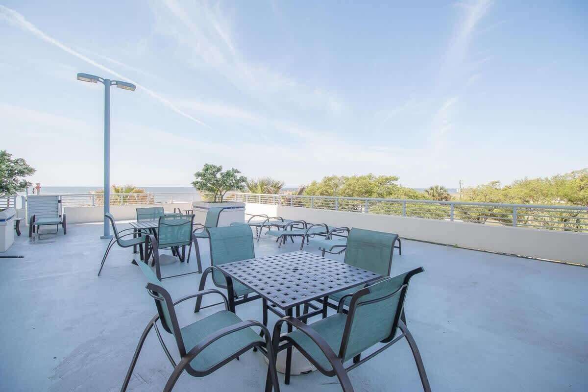 An outdoor patio with tables and chairs, a street lamp, and a view of the sea.