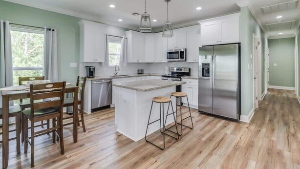 Una cocina moderna con armarios blancos, electrodomésticos de acero inoxidable y una mesa de comedor de madera con sillas.