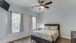 Un dormitorio con cama, ventilador de techo y dos ventanas.
