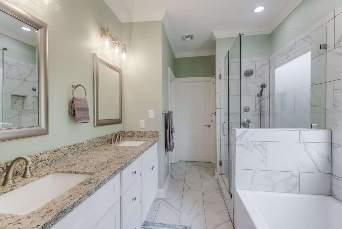 A bathroom with a double sink, a large mirror, a glass shower enclosure, and a white bathtub.