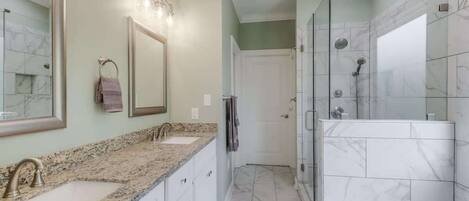 A bathroom with a double sink, a large mirror, a glass shower enclosure, and a white bathtub.