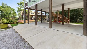 Un espacio al aire libre techado con piso de concreto, pilares de madera y vista a un lago.