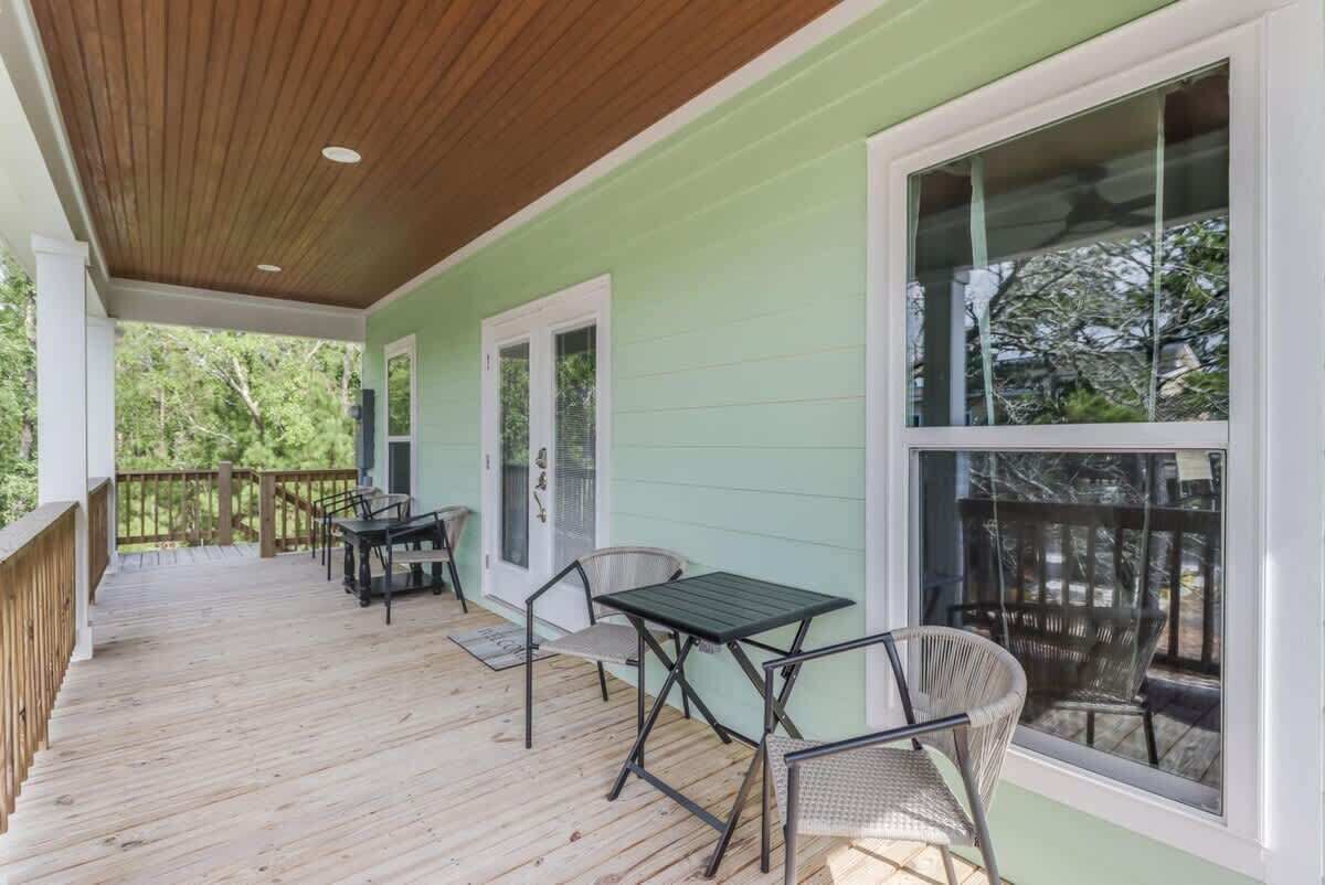 A covered porch with a wooden ceiling, a green wall, and a table with chairs.