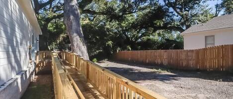 A fenced backyard with a wooden deck, a large tree, and a white house.