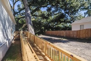 Ein umzäunter Garten mit einer Holzterrasse, einem großen Baum und einem weißen Haus.