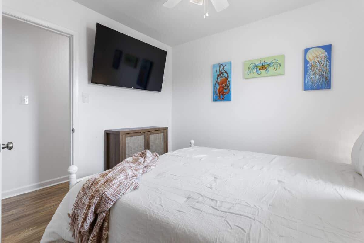 A bedroom with a bed, a TV mounted on the wall, and three paintings.
