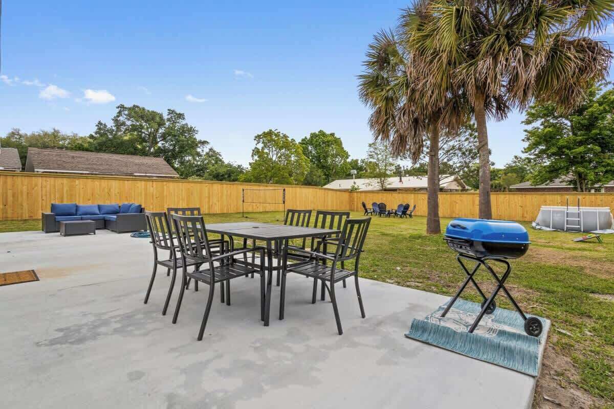 A backyard with a patio table, chairs, a grill, and a wooden fence.