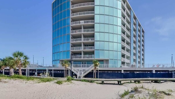 A modern, multi-story hotel with a curved facade, balconies, and a covered walkway. - Sunsets From The Sandy Balcony (Biloxi)