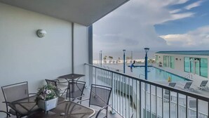 A balcony with a pool view, metal chairs, a table, and a potted plant. - Sunsets From The Sandy Balcony (Biloxi)