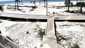 A beach view with a wooden boardwalk, palm trees, and a clear sky. - Sunsets From The Sandy Balcony (Biloxi)