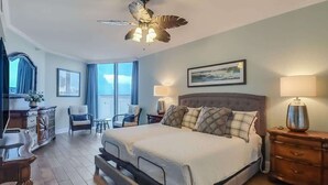 A bedroom with a bed, a ceiling fan, a nightstand, a lamp, a chair, a dresser, and a window with curtains. - Sunsets From The Sandy Balcony (Biloxi)