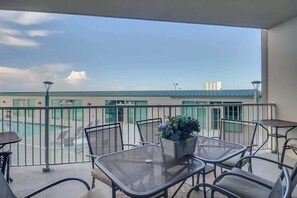 A balcony with outdoor seating, a potted plant, and a view of buildings in the distance. - Sunsets From The Sandy Balcony (Biloxi)