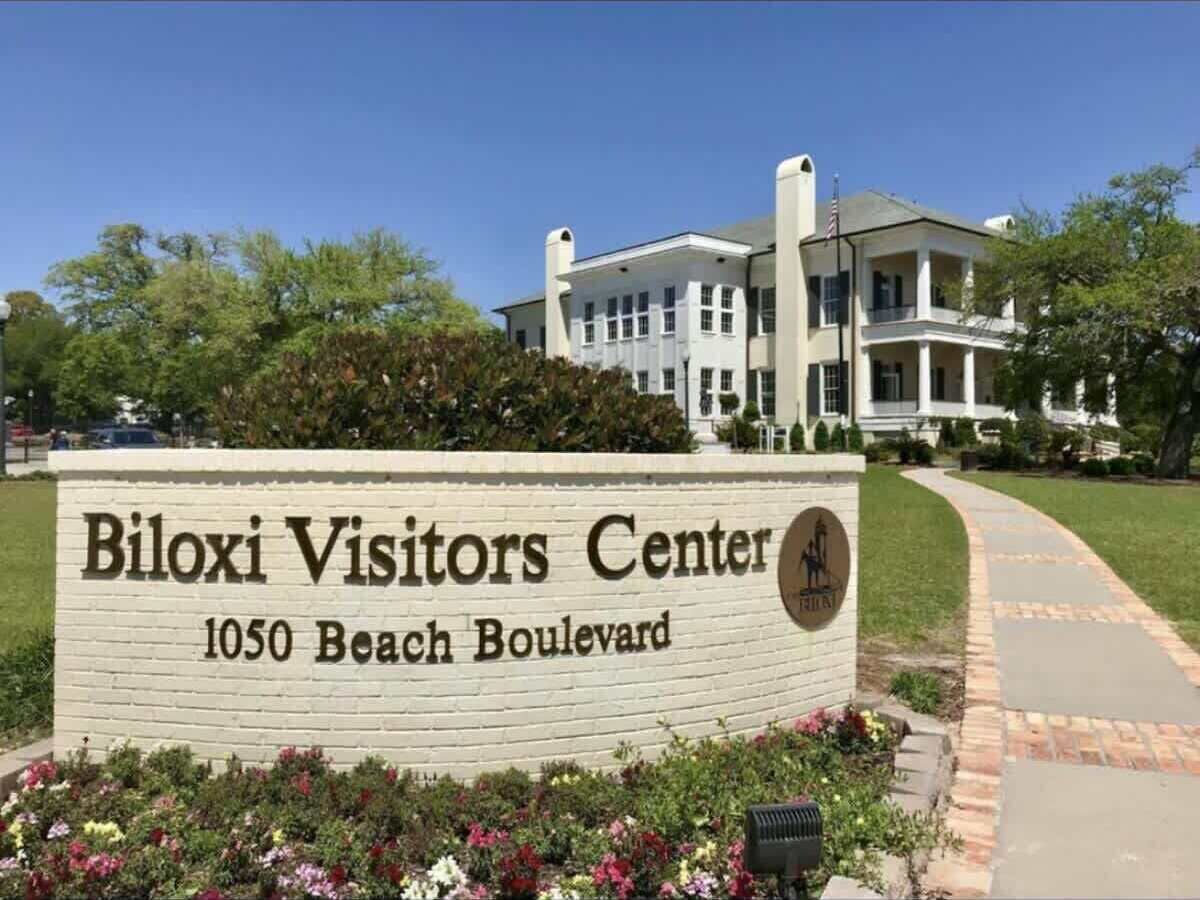 Cartell del Centre de Visitants de Biloxi a l'avinguda Beach, 1050, amb un edifici gran al fons.