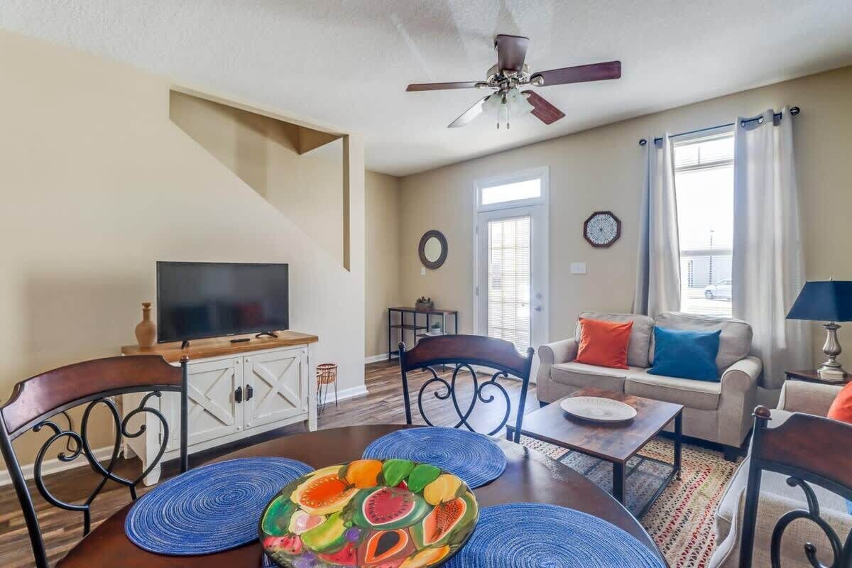 Una sala de estar con televisor, sofá, mesa de centro y mesa de comedor con individuales.