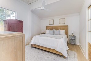 A bedroom with a wooden bed, bedside tables, a ceiling fan, and a window. - Chelle's in Bay St. Louis (Bay St Louis)