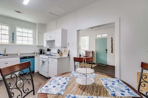 Uma cozinha moderna com armários brancos, lava-louças azul e um espaço de refeições com mesa de mármore e jogos americanos estampados.