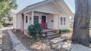 A single-story house with a red door, a covered porch, and a small front yard with a tree and shrubs. - Miazza Cottage in Gulfport (Gulfport)