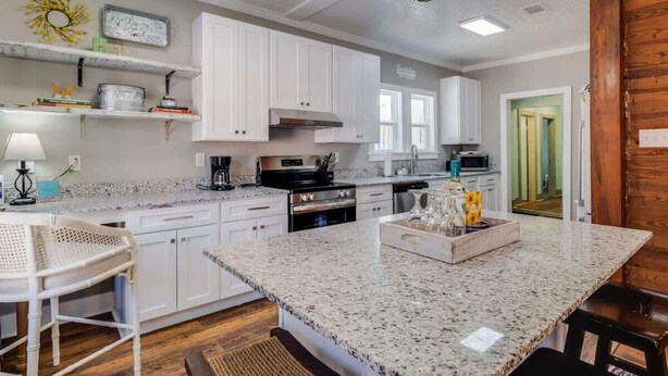 A kitchen with white cabinets, granite countertops, a central island, and a hanging light fixture. - Miazza Cottage in Gulfport (Gulfport)