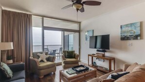 A living room with a sofa, chairs, a coffee table, a TV, and a ceiling fan. - Endless Blue at the Gulf Watch (Biloxi)