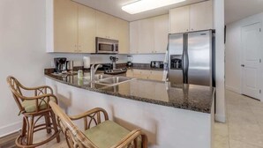 A modern kitchen with a central island, stainless steel appliances, and light-colored cabinetry. - Endless Blue at the Gulf Watch (Biloxi)
