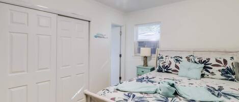 A bedroom with a bed, a nightstand, a window with blinds, and a ceiling fan.