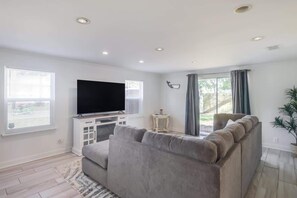 A modern living room with a flat-screen TV, grey sofa, and a small side table. - The Magnolia Retreat (Gulfport)