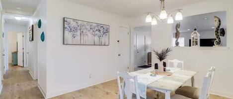 Un comedor con una mesa y sillas blancas, una araña y un cuadro en la pared.