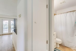 A bathroom with a white toilet, a shower curtain, and a window with curtains. - The Magnolia Retreat (Gulfport)