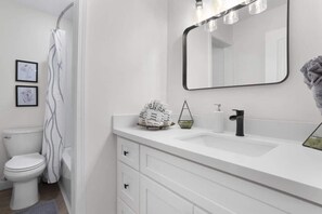 A bathroom with a white sink, a mirror, and a toilet. - The Seabreeze Bungalow (Ocean Springs)