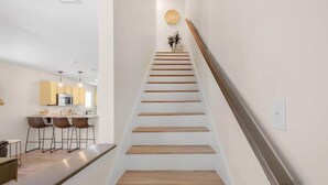 A modern interior with a staircase leading to a landing, a kitchen area with bar stools, and a dining table. - Cozy 2 Bed Duplex Just Blocks From Downtown Biloxi! (Biloxi)