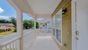 A covered porch with a white railing, a door with a window, and a view of a residential street. - Cozy 2 Bed Duplex Just Blocks From Downtown Biloxi! (Biloxi)