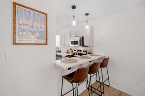 Una cocina moderna con encimera blanca, taburetes de bar e iluminación colgante.
