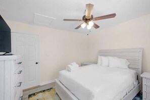 Un dormitorio con cama, ventilador de techo, cómoda blanca y una puerta.