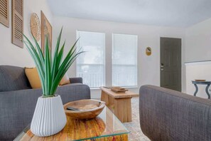 Una sala de estar con un sofá, una mesa baja con un cuenco, una planta en maceta y una puerta.
