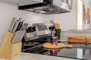Uma cozinha com fogão de aço inoxidável, suporte de facas, tábua de corte de madeira e um recipiente verde.