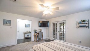 A bedroom with a bed, a desk, a chair, a television, and a ceiling fan. - Cottage on Broadmoor (Gulfport)