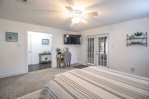 A bedroom with a bed, a desk, a chair, a television, and a ceiling fan. - Cottage on Broadmoor (Gulfport)